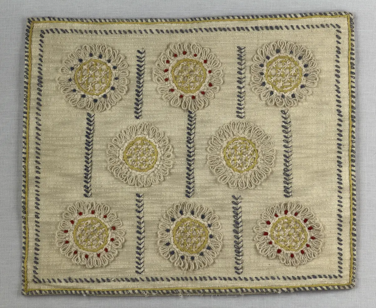 Kuddvar, gjord av tuskaftsväv i bomull och cottolin, som är dekorerad på framsidan med broderi utfört med ullgarn och splendolin i stjälksöm, kedjesöm, bottensöm, läggsöm, trädsöm, knutar samt ryaknutar. Kuddvaret är hopsytt med raksöm, därefter ett varv med stjälksöm cirka 1cm in från ytterkanten på kuddvarets rätsida.