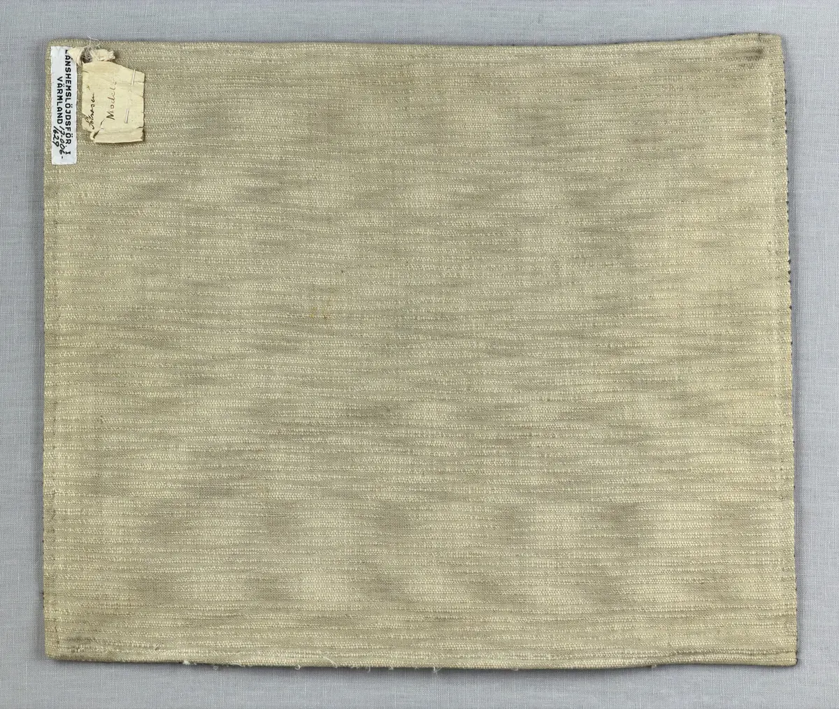 Kuddvar, gjord av tuskaftsväv i bomull och cottolin, som är dekorerad på framsidan med broderi utfört med ullgarn och splendolin i stjälksöm, kedjesöm, bottensöm, läggsöm, trädsöm, knutar samt ryaknutar. Kuddvaret är hopsytt med raksöm, därefter ett varv med stjälksöm cirka 1cm in från ytterkanten på kuddvarets rätsida.