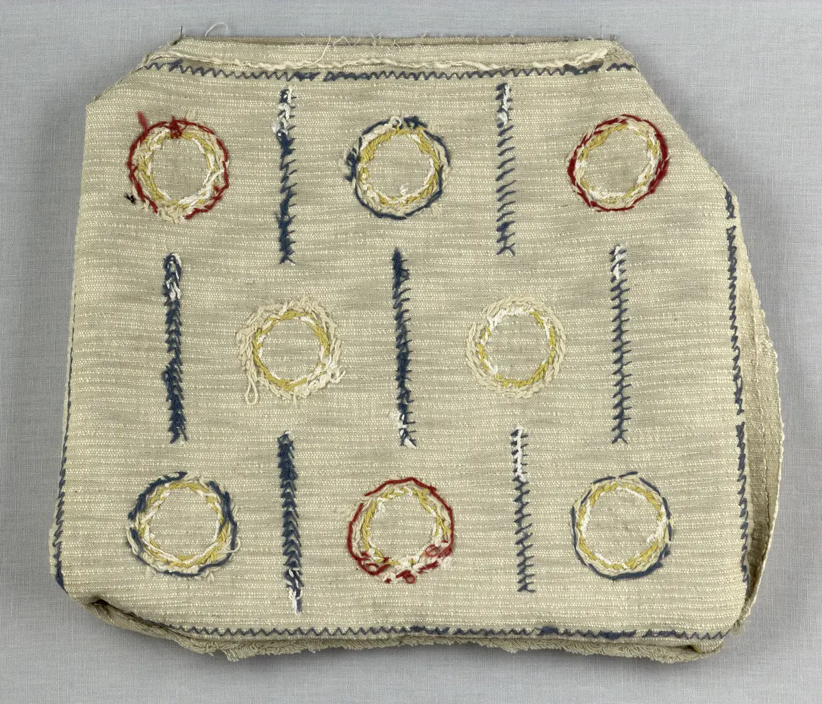 Kuddvar, gjord av tuskaftsväv i bomull och cottolin, som är dekorerad på framsidan med broderi utfört med ullgarn och splendolin i stjälksöm, kedjesöm, bottensöm, läggsöm, trädsöm, knutar samt ryaknutar. Kuddvaret är hopsytt med raksöm, därefter ett varv med stjälksöm cirka 1cm in från ytterkanten på kuddvarets rätsida.