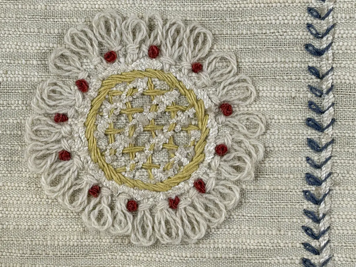 Kuddvar, gjord av tuskaftsväv i bomull och cottolin, som är dekorerad på framsidan med broderi utfört med ullgarn och splendolin i stjälksöm, kedjesöm, bottensöm, läggsöm, trädsöm, knutar samt ryaknutar. Kuddvaret är hopsytt med raksöm, därefter ett varv med stjälksöm cirka 1cm in från ytterkanten på kuddvarets rätsida.