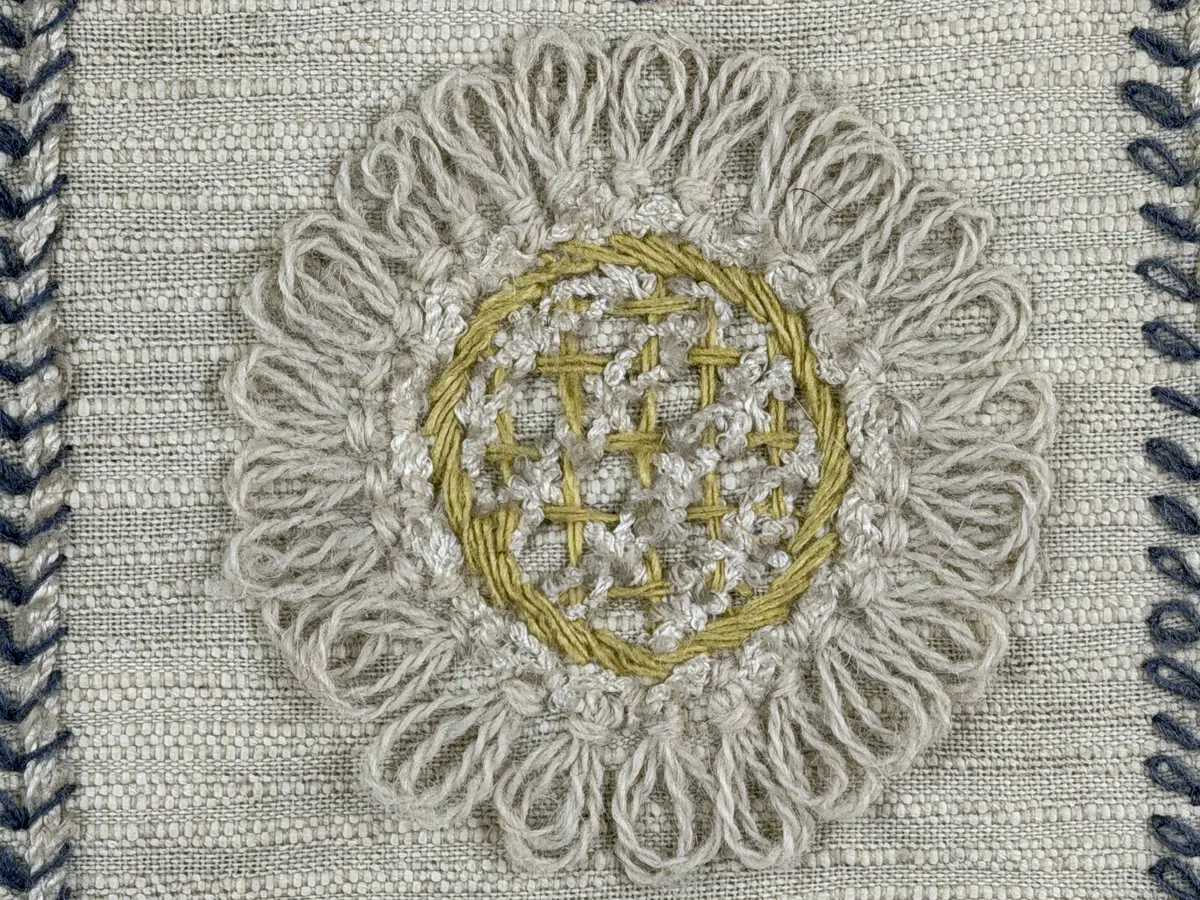 Kuddvar, gjord av tuskaftsväv i bomull och cottolin, som är dekorerad på framsidan med broderi utfört med ullgarn och splendolin i stjälksöm, kedjesöm, bottensöm, läggsöm, trädsöm, knutar samt ryaknutar. Kuddvaret är hopsytt med raksöm, därefter ett varv med stjälksöm cirka 1cm in från ytterkanten på kuddvarets rätsida.