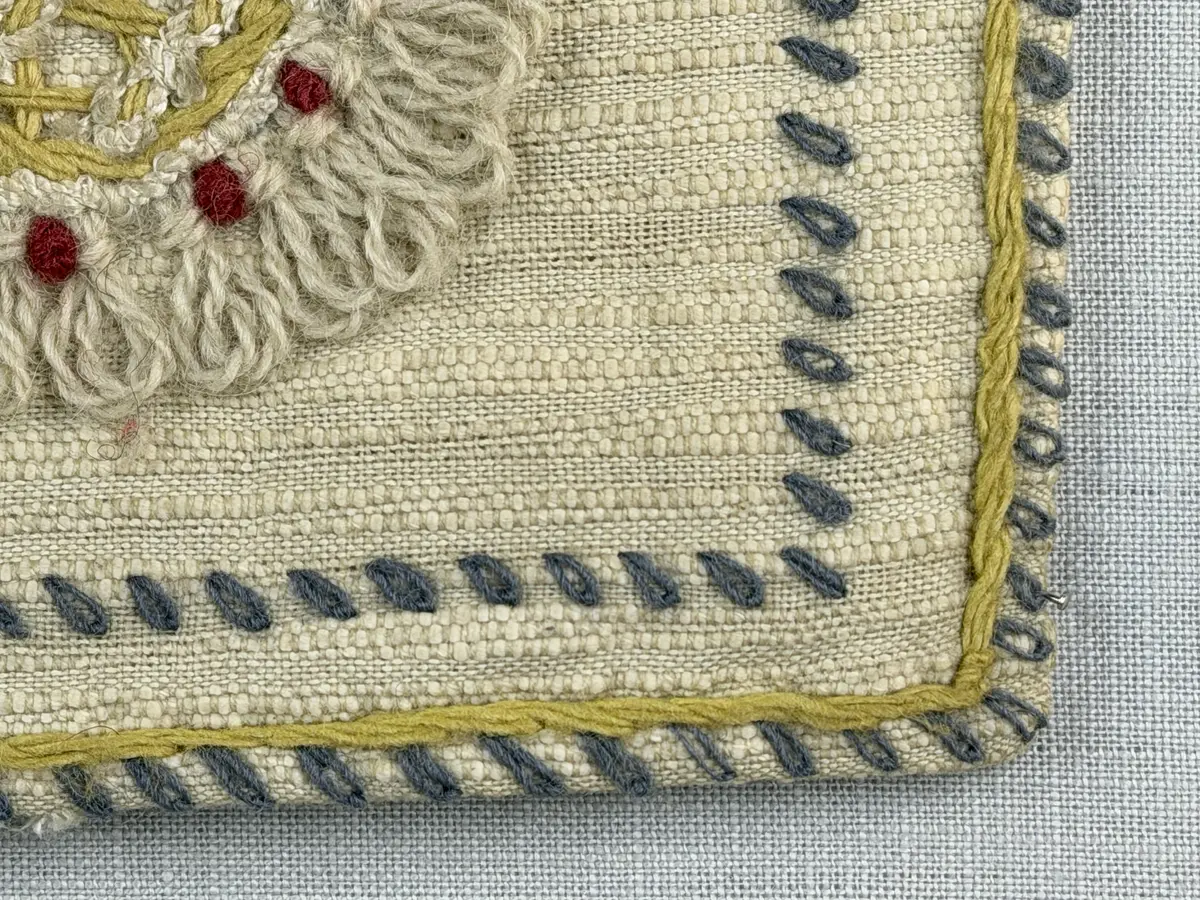 Kuddvar, gjord av tuskaftsväv i bomull och cottolin, som är dekorerad på framsidan med broderi utfört med ullgarn och splendolin i stjälksöm, kedjesöm, bottensöm, läggsöm, trädsöm, knutar samt ryaknutar. Kuddvaret är hopsytt med raksöm, därefter ett varv med stjälksöm cirka 1cm in från ytterkanten på kuddvarets rätsida.