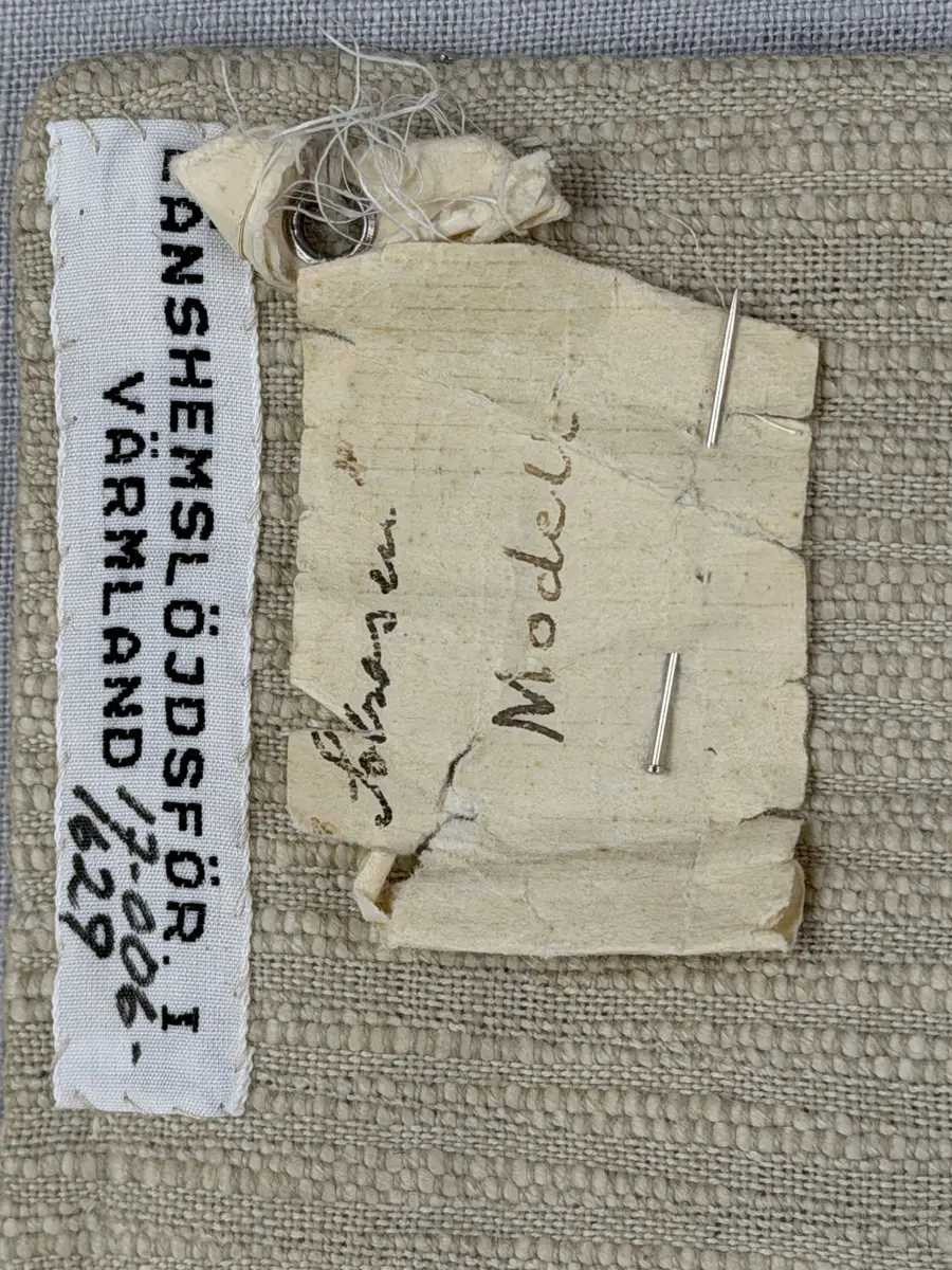 Kuddvar, gjord av tuskaftsväv i bomull och cottolin, som är dekorerad på framsidan med broderi utfört med ullgarn och splendolin i stjälksöm, kedjesöm, bottensöm, läggsöm, trädsöm, knutar samt ryaknutar. Kuddvaret är hopsytt med raksöm, därefter ett varv med stjälksöm cirka 1cm in från ytterkanten på kuddvarets rätsida.