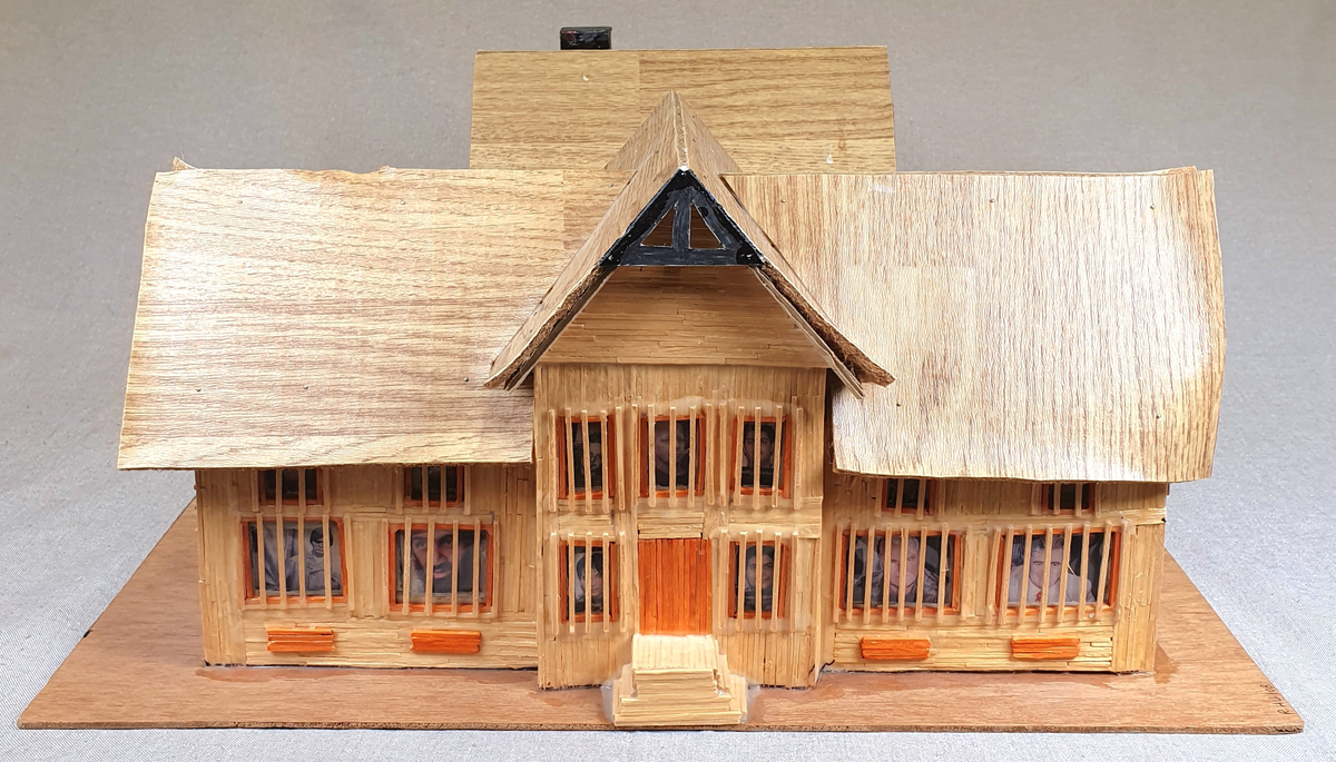 Målestokkmodell av Molde fengsel limt til en treplate. Bygget av finerplater, fyrstikker, papp, vinylbelegg, plast og tekstil. I vinduene i det fremste bygget er det bilder av forskjellige folk, blant annet hijackere tilknyttet 9/11 som var de eneste bildene med navn under.