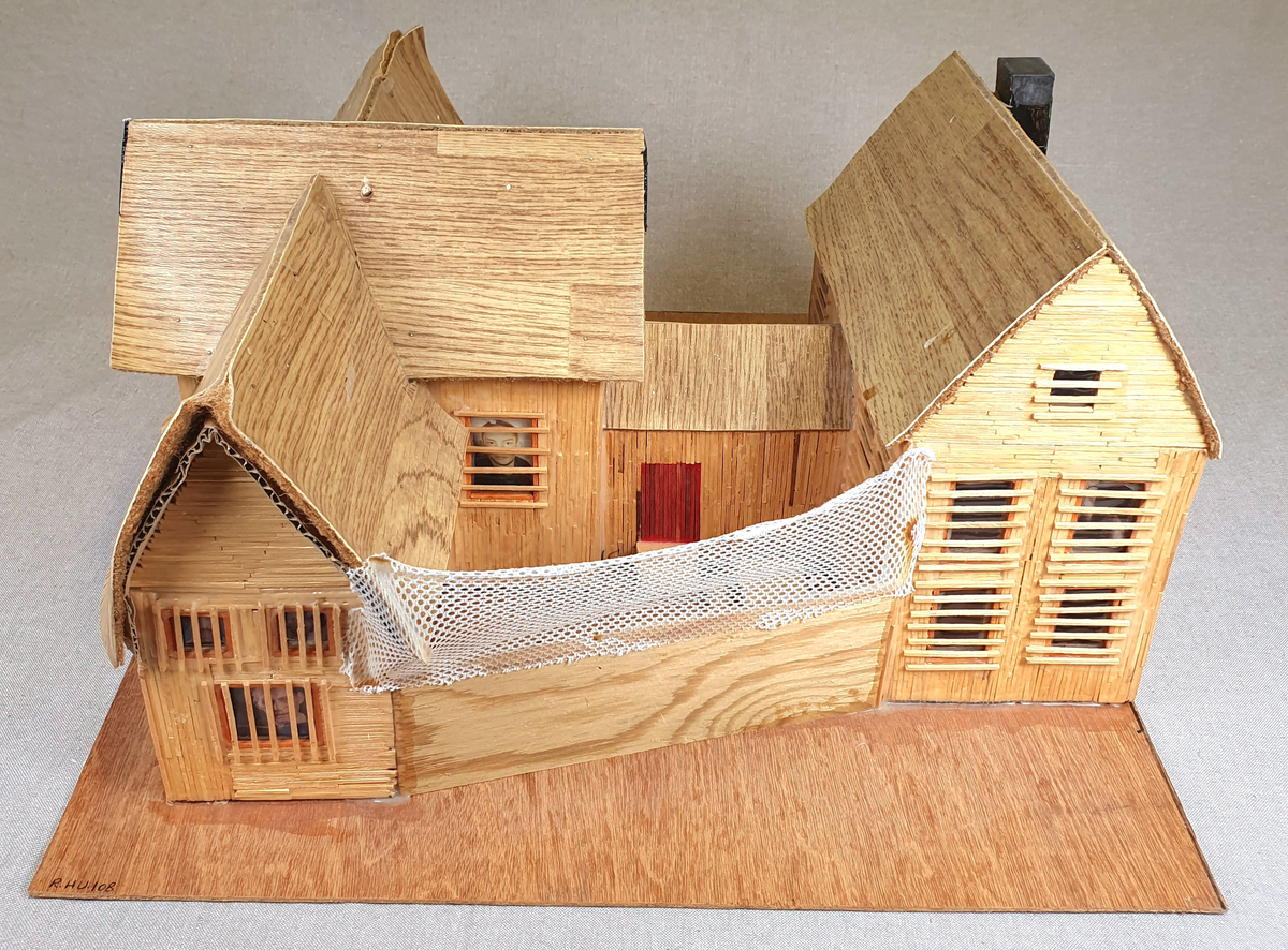 Målestokkmodell av Molde fengsel limt til en treplate. Bygget av finerplater, fyrstikker, papp, vinylbelegg, plast og tekstil. I vinduene i det fremste bygget er det bilder av forskjellige folk, blant annet hijackere tilknyttet 9/11 som var de eneste bildene med navn under.