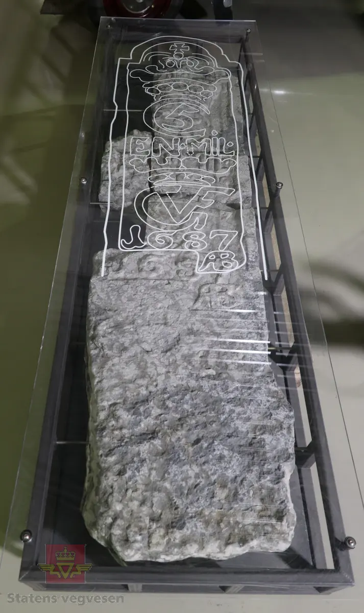 Grå kalkstein i 5 deler. Noe av monogrammet er borte, men 1687 er godt synelig. Kun den største delen er merket. Steinen er lagret på to paller.
