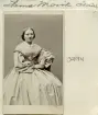 Porträtt av fröken Hanna Movik. Född i Västervik 1837 kom hon från 1859 som mamsell att ingå i Carl Johan Ajaxsons hushåll i dennes säteri i Vårdsberg. Från 1863 bodde hon hos sin bror, brukskassören Werner Movik i Åtvidaberg. Här blev hon kvar till det nya seklets inträde. År 1901, några år efter broderns död, flyttade hon till brorsdotterns hushåll i Vetlanda. När den yngre släktingens make erbjöds tjänsten som provilialläkare i Ekeby, flyttade Hanna med. Hennes liv ändades där av hjärtfel i kombination med lunginflammation den 25 januari 1910. Foto omkring 1870.