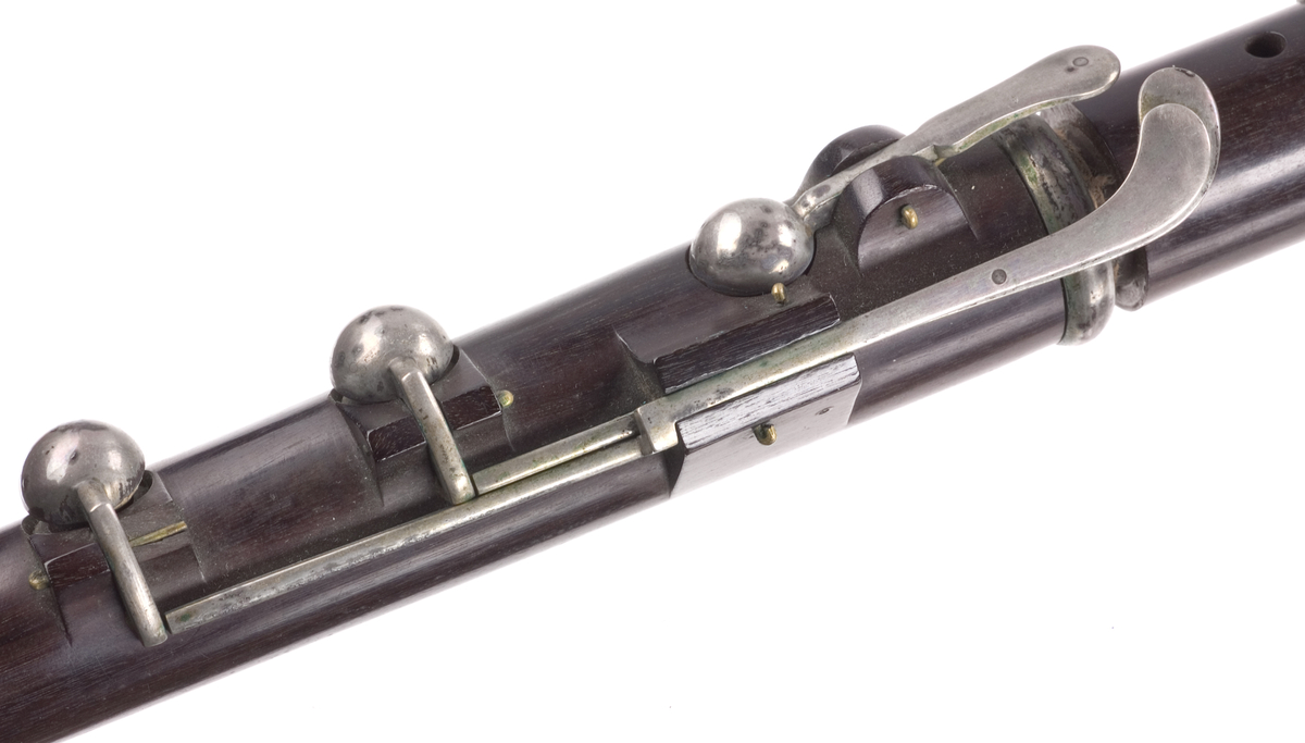 Tvärflöjt i ebenholts med silverringar. Nedersta ringen saknas. 5 delar. Konisk form. Sprickor i munstycke och päron. Stämpel på oval silverplatta på päronet. C-fot. 8 klaffar i silver med bocklagring och kulformade plattor. 