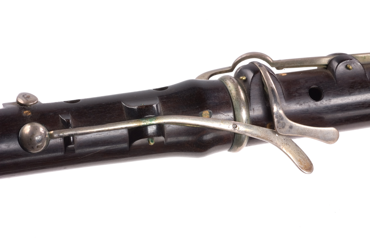 Tvärflöjt i ebenholts med silverringar. Nedersta ringen saknas. 5 delar. Konisk form. Sprickor i munstycke och päron. Stämpel på oval silverplatta på päronet. C-fot. 8 klaffar i silver med bocklagring och kulformade plattor. 