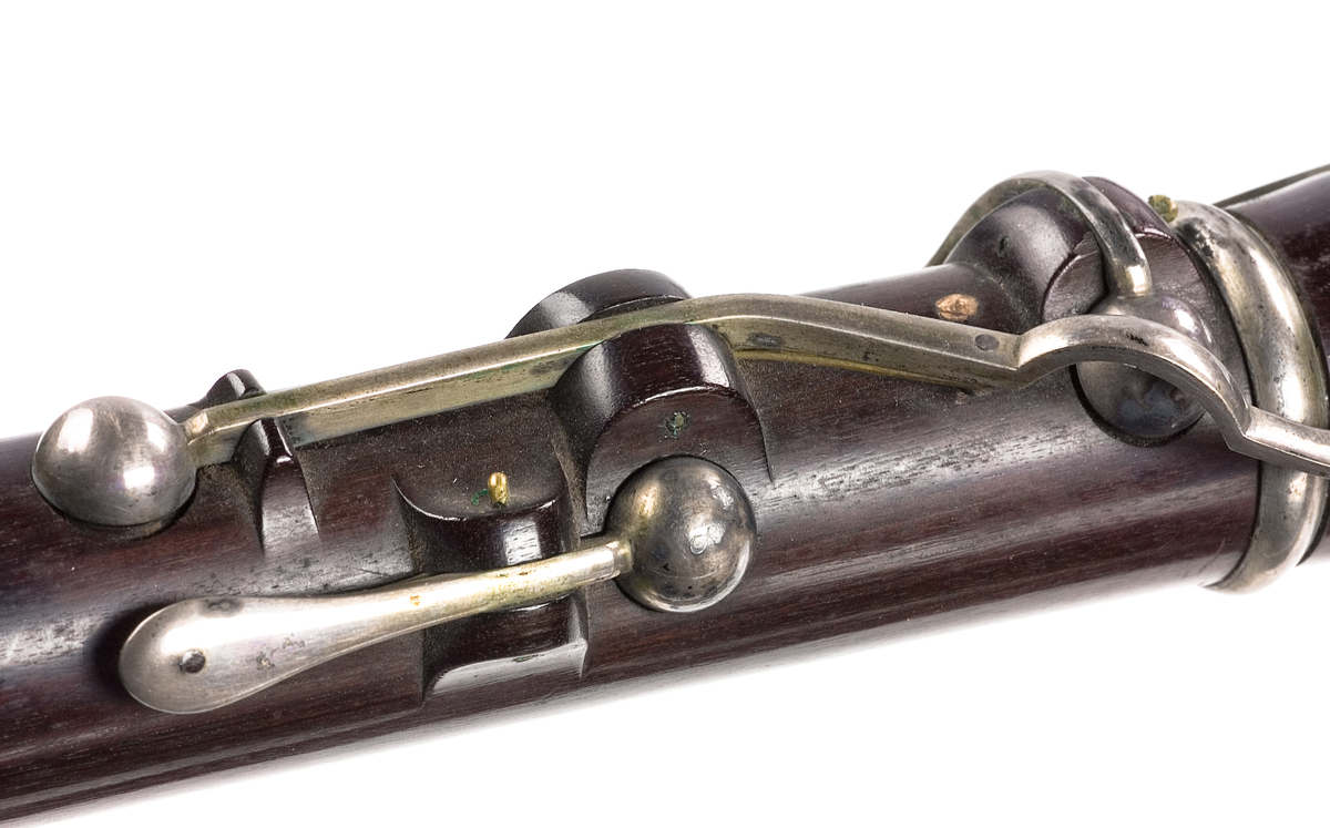 Tvärflöjt i ebenholts med silverringar. Nedersta ringen saknas. 5 delar. Konisk form. Sprickor i munstycke och päron. Stämpel på oval silverplatta på päronet. C-fot. 8 klaffar i silver med bocklagring och kulformade plattor. 