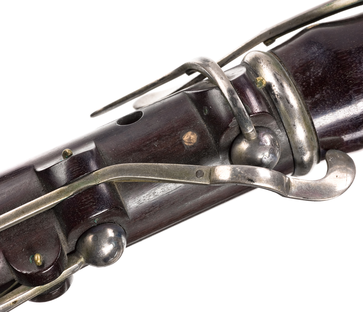 Tvärflöjt i ebenholts med silverringar. Nedersta ringen saknas. 5 delar. Konisk form. Sprickor i munstycke och päron. Stämpel på oval silverplatta på päronet. C-fot. 8 klaffar i silver med bocklagring och kulformade plattor. 