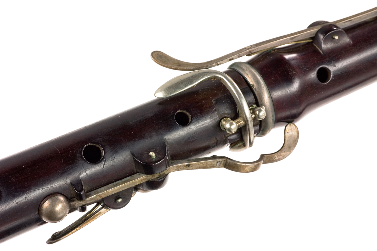 Tvärflöjt i ebenholts med silverringar och C-fot. 5 delar. Konisk form och svarvade vulster. Stämpel på oval silverplatta på päronet. C-fot. 8 klaffar med bocklagring, varav 1 klaff är trasig. 1 bocklagring är ersatt med kullagring.