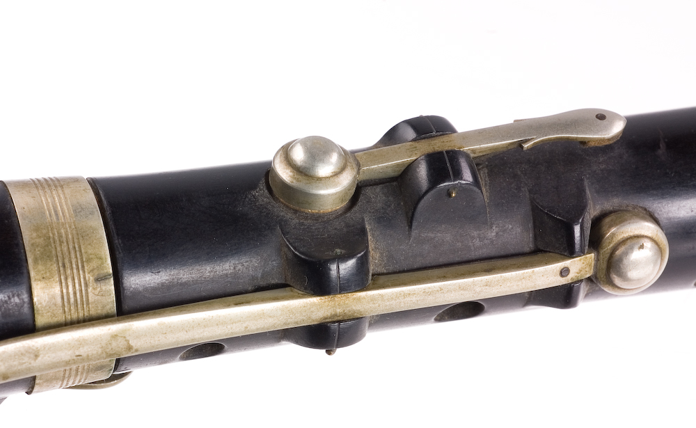 Tvärflöjt i ebenholts med ringar av silver. Nedersta ringen saknas. 5 delar. Sprickor i munstycke och päron. C-fot. 8 klaffar med bocklagring och tjocka runda plattor med kulformade toppar. Delar av lägsta klaffen och dess lagring saknas.