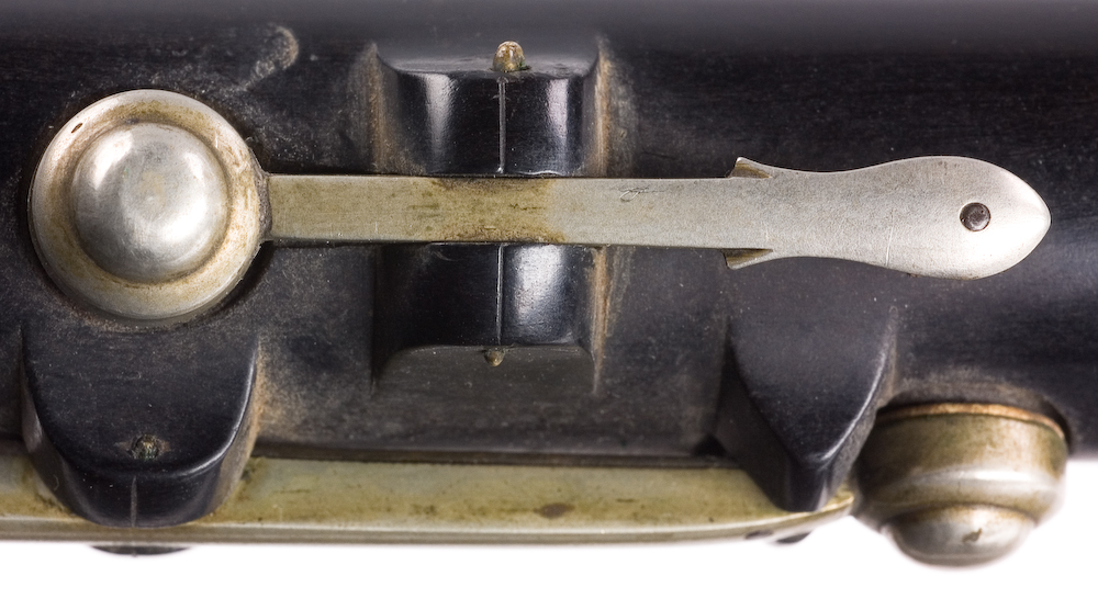 Tvärflöjt i ebenholts med ringar av silver. Nedersta ringen saknas. 5 delar. Sprickor i munstycke och päron. C-fot. 8 klaffar med bocklagring och tjocka runda plattor med kulformade toppar. Delar av lägsta klaffen och dess lagring saknas.