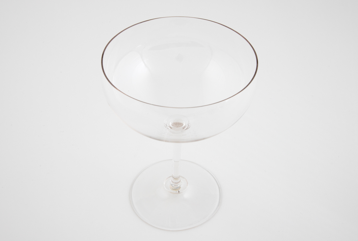 Drikkeglass i klart glass. Lav og vid kupa, som hviler på en smal stett. Sirkulær fotplate, noe hevet på midten. Overgangen mellom fot, stett og kupa er markert med ringformede vulster.
