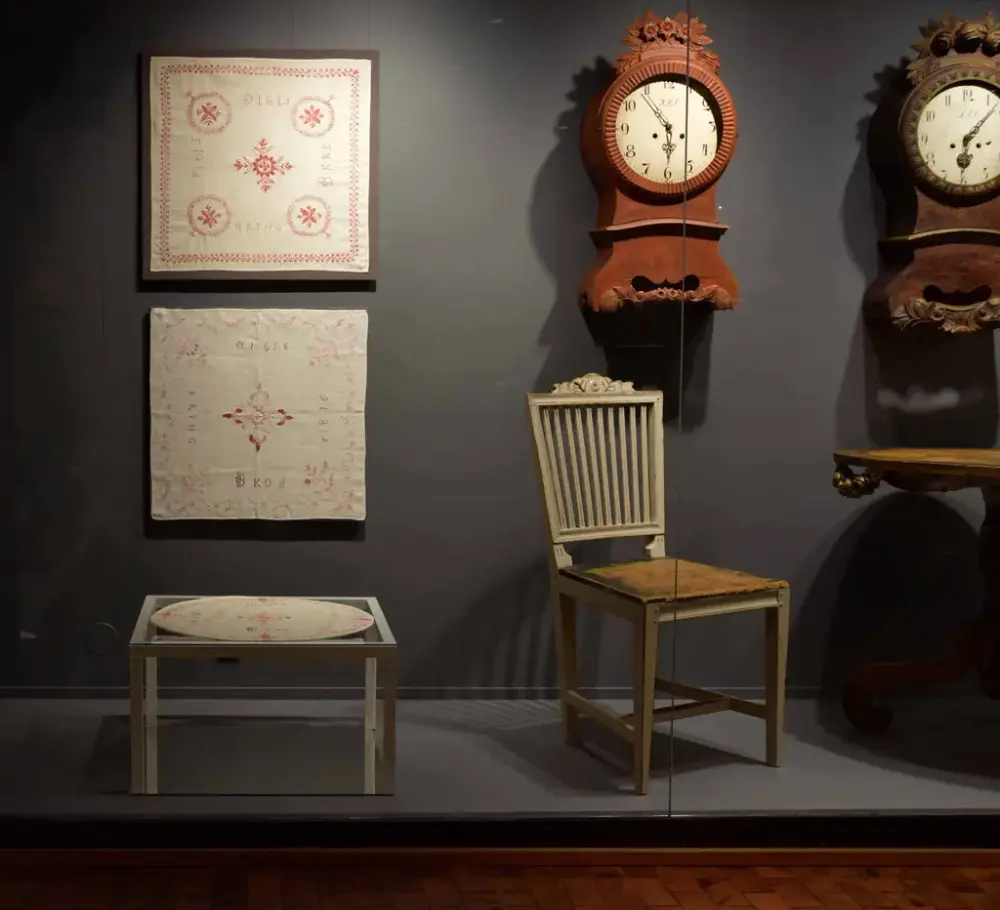 Utställnignsmonter från Händers verk; snidade väggur, möbler samt broderade dukar.