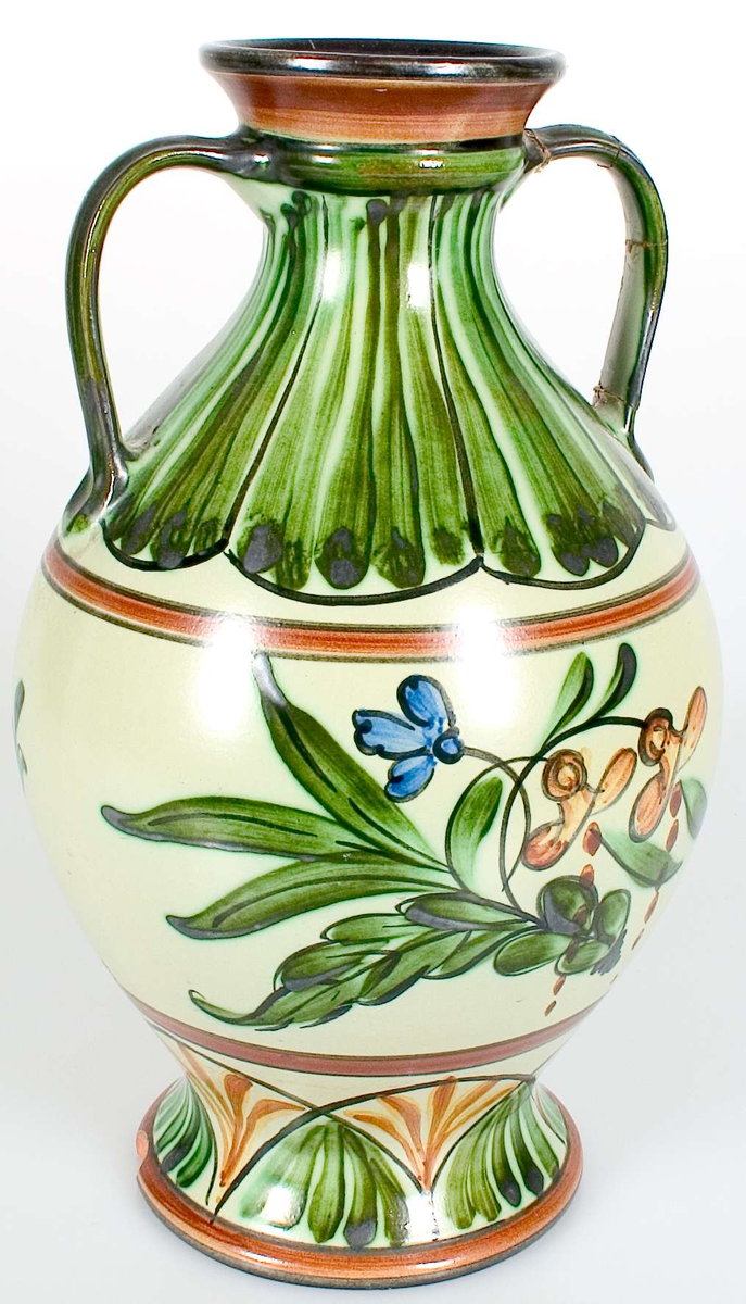 Vas med två hänklar. Ena hänkeln skadad på flera ställen, fastlimmad. Bit bortslagen på foten.