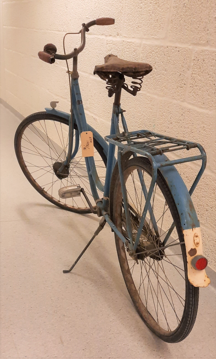 Sykkel. Blå DBS. Damesykkel. Lèr sete. Ringeklokke på styret. Handbrems. DBS merke framme på styrestang. Gummi handtak på styret.