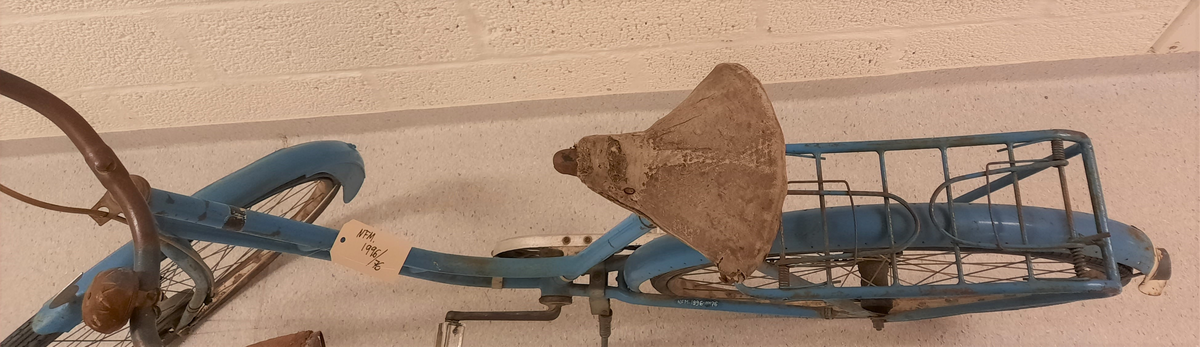 Sykkel. Blå DBS. Damesykkel. Lèr sete. Ringeklokke på styret. Handbrems. DBS merke framme på styrestang. Gummi handtak på styret.