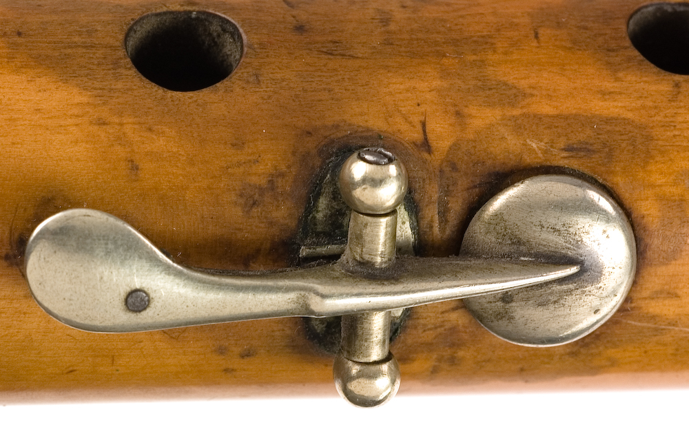 Tvärflöjt i buxbom med silverringar. 5 delar. C-fot. Kvadratiskt anblåsningshål. Tydliga märken efter användning vid anblåsnings- och fingerhål. 10 klaffar med kullagring, fästa i fastskruvade plattor. Klaffarnas plattor är runda. Klaffhålen har monterade metallrör.