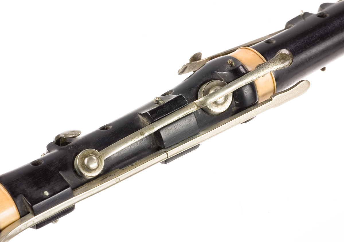 Tvärflöjt i ebenholts med ringar i elfenben. 5 delar. H-fot. Sprickor i munstycke och päron. 10 klaffar med bock- och vulstlagring. Klaffarna har runda, tämligen tjocka, plattor med en rundad upphöjning i mitten.