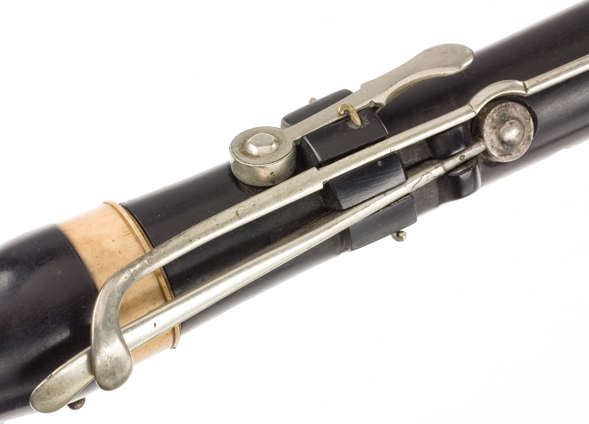 Tvärflöjt i ebenholts med ringar i elfenben. 5 delar. H-fot. Sprickor i munstycke och päron. 10 klaffar med bock- och vulstlagring. Klaffarna har runda, tämligen tjocka, plattor med en rundad upphöjning i mitten.