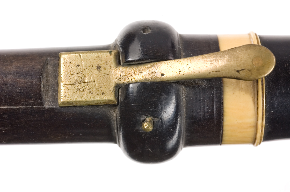 Tvärflöjt i ebenholts med ringar i elfenben. Kortare flöjt, troligtvis stämd i Eb eller F. 4 delar. Ovalt anblåsningshål. 2 klaffar, den övre med bocklagring, den lägre med vulstlagrin. Kvadratiska plattor.