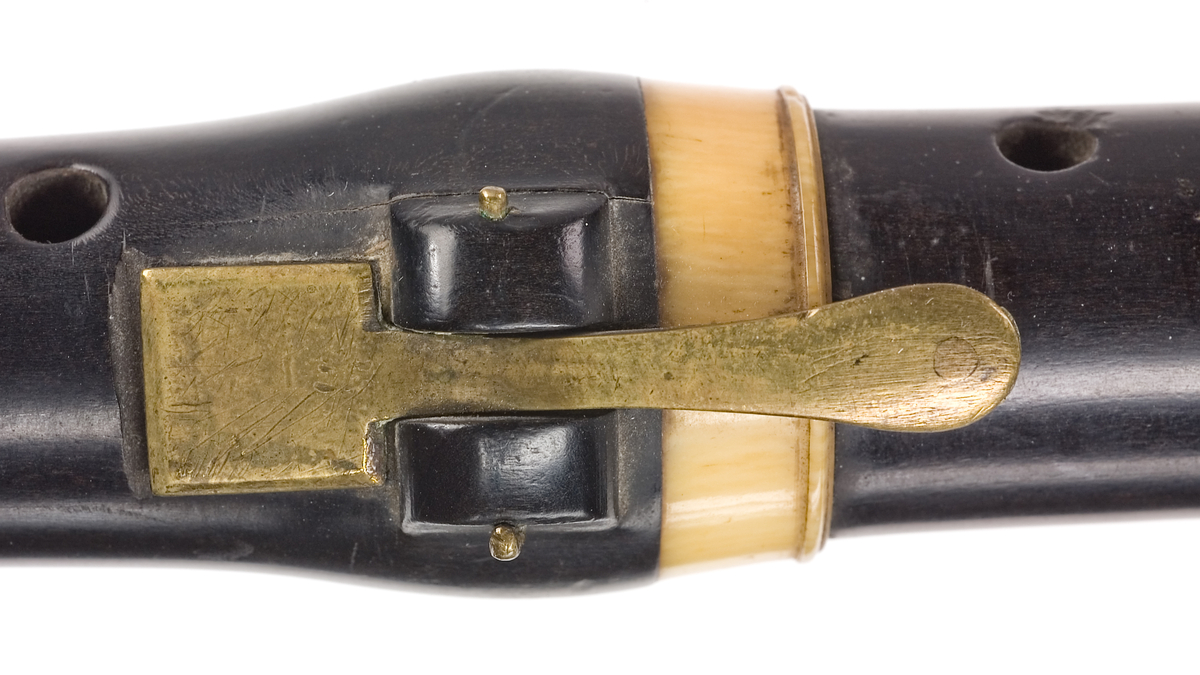 Tvärflöjt i ebenholts med ringar i elfenben. Kortare flöjt, troligtvis stämd i Eb eller F. 4 delar. Ovalt anblåsningshål. 2 klaffar, den övre med bocklagring, den lägre med vulstlagrin. Kvadratiska plattor.