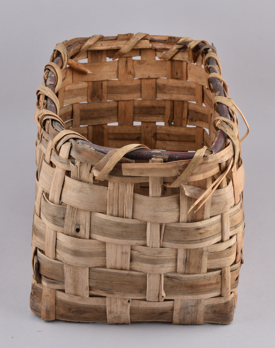 Korg i rakflätad spån. Kantens vidja är lindad. Rektangulär form med flätad botten.