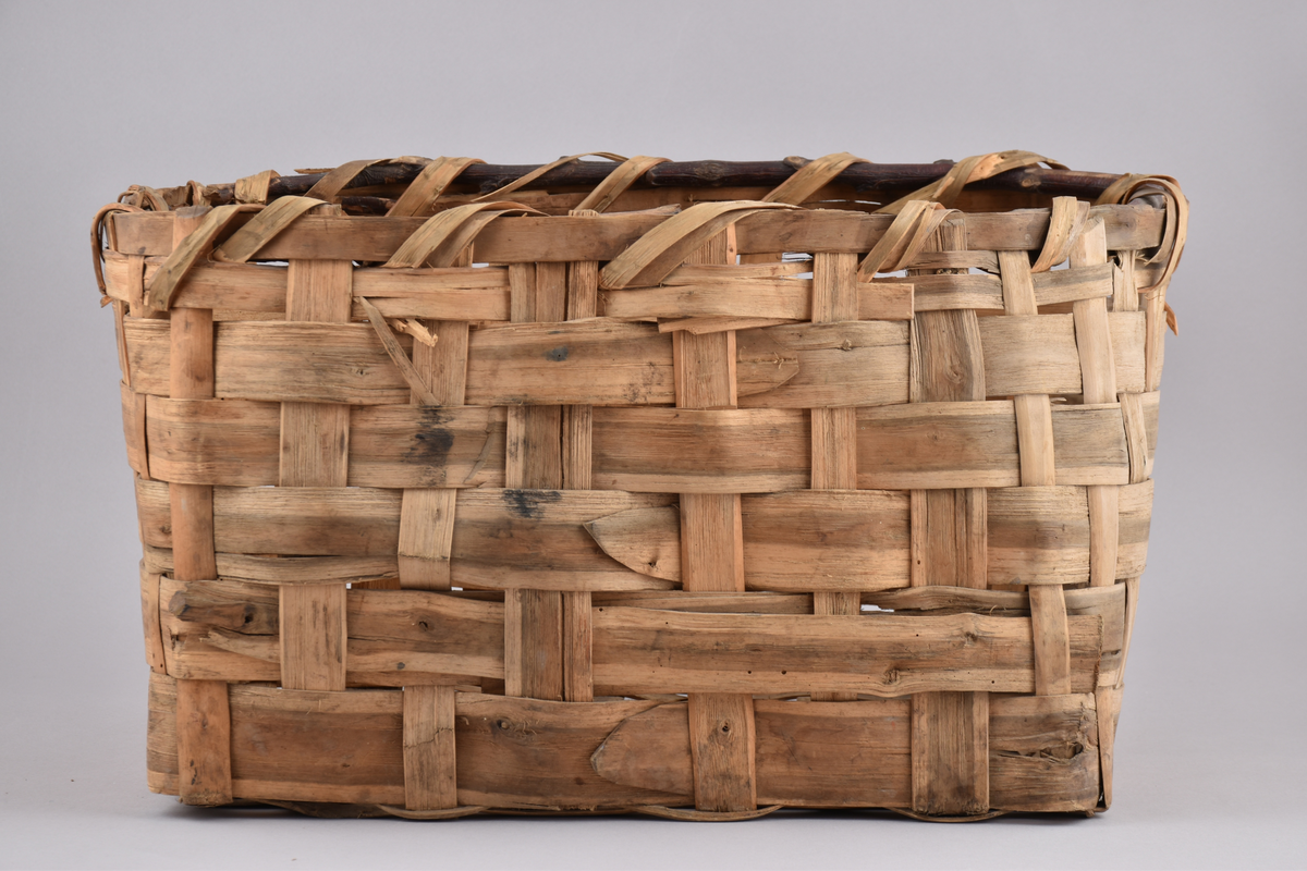Korg i rakflätad spån. Kantens vidja är lindad. Rektangulär form med flätad botten.