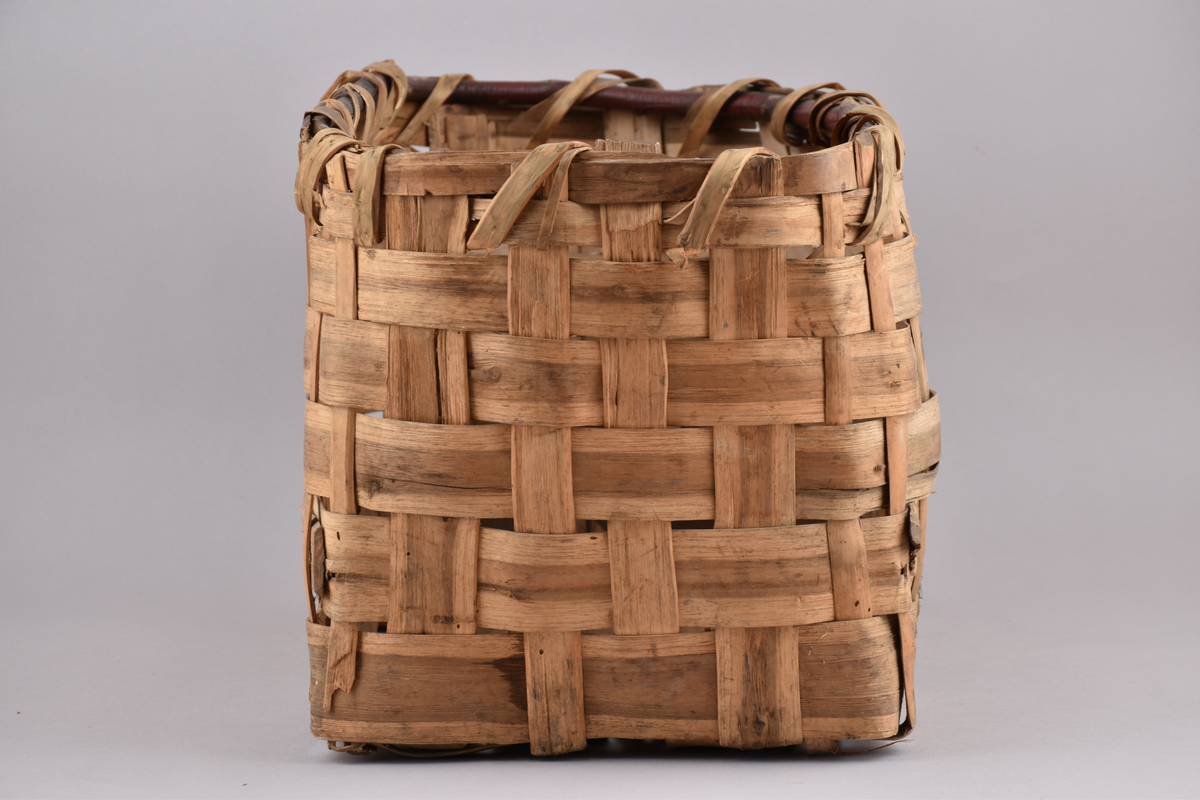 Korg i rakflätad spån. Kantens vidja är lindad. Rektangulär form med flätad botten.