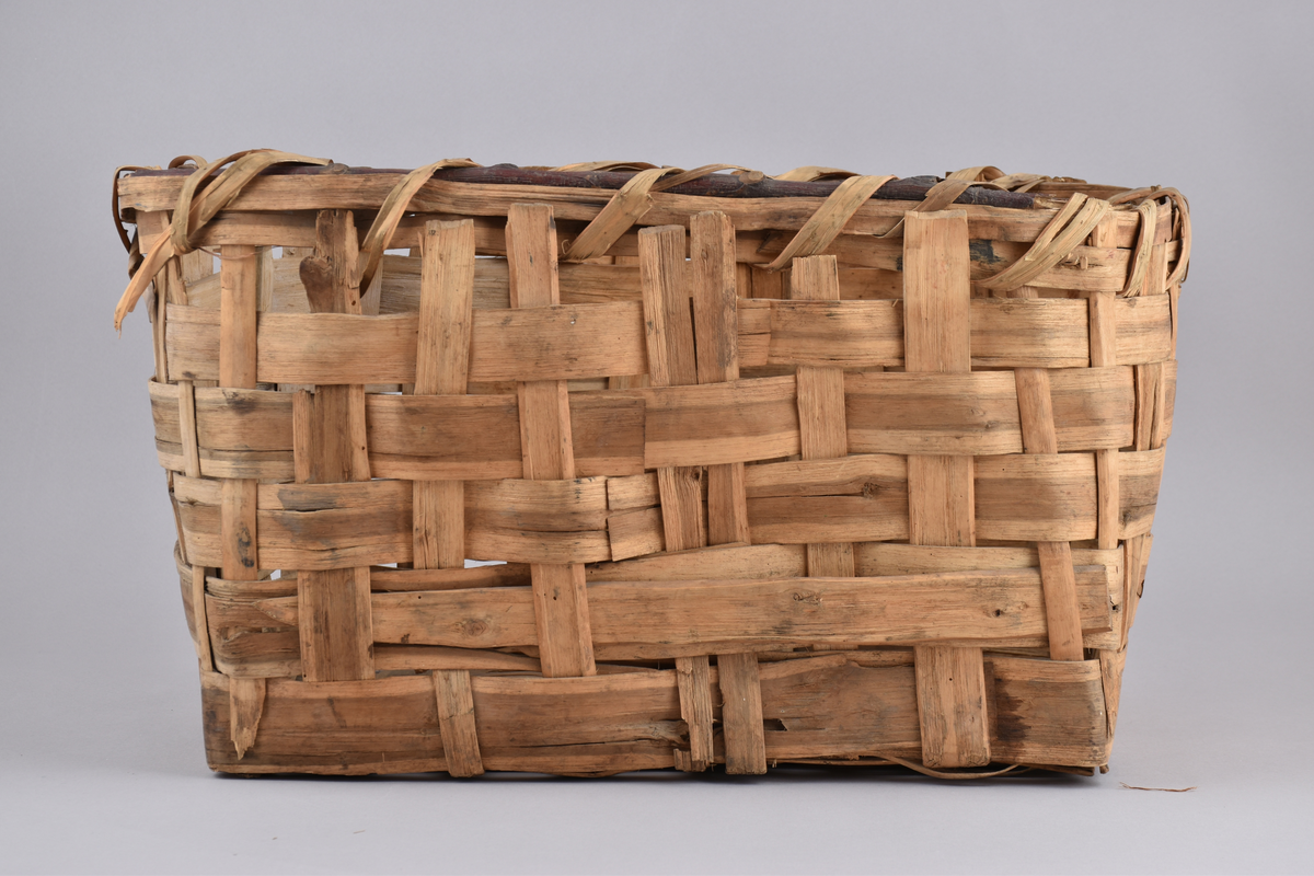 Korg i rakflätad spån. Kantens vidja är lindad. Rektangulär form med flätad botten.