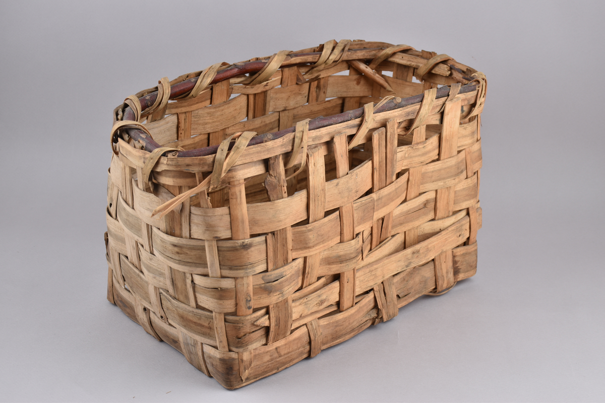 Korg i rakflätad spån. Kantens vidja är lindad. Rektangulär form med flätad botten.