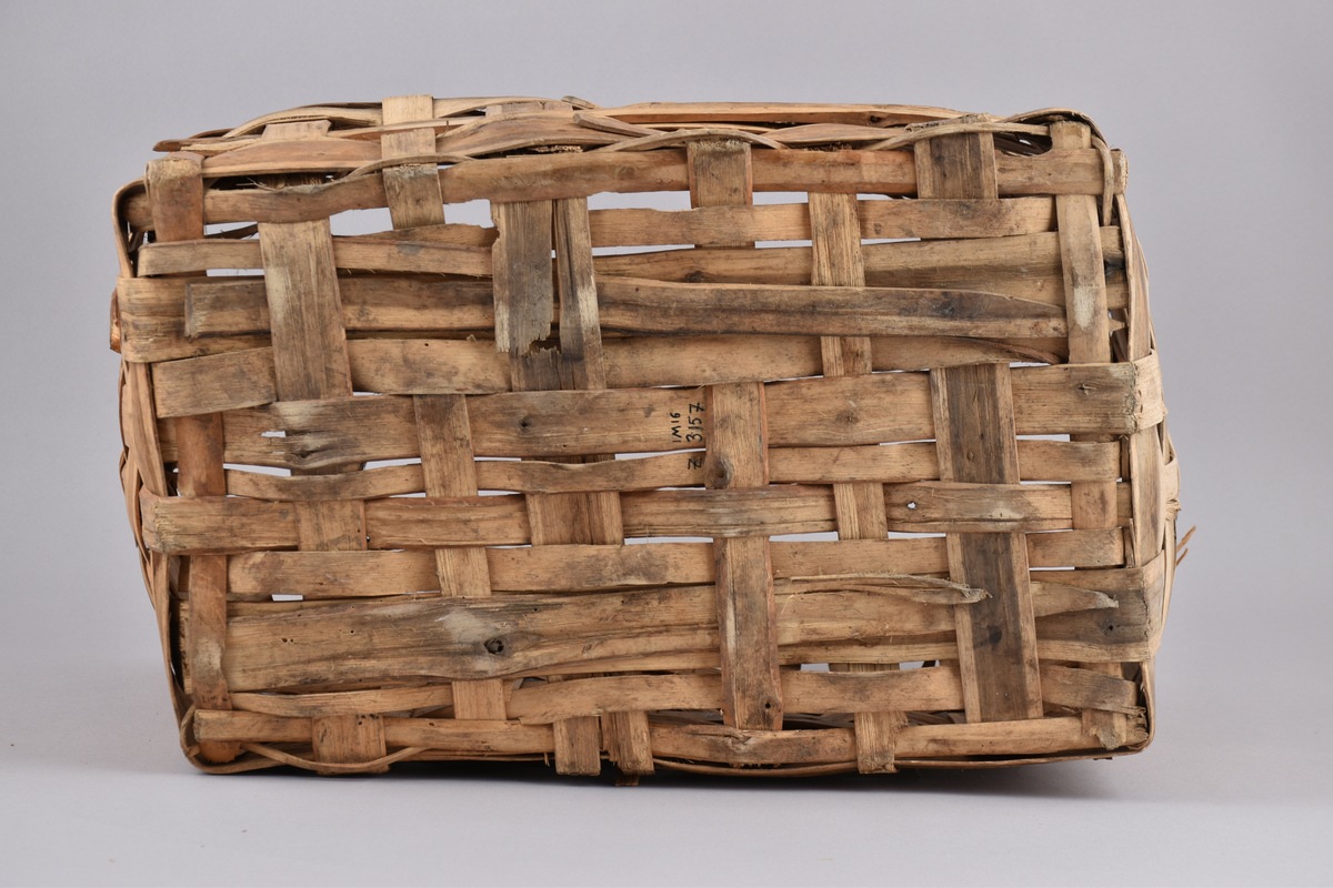 Korg i rakflätad spån. Kantens vidja är lindad. Rektangulär form med flätad botten.