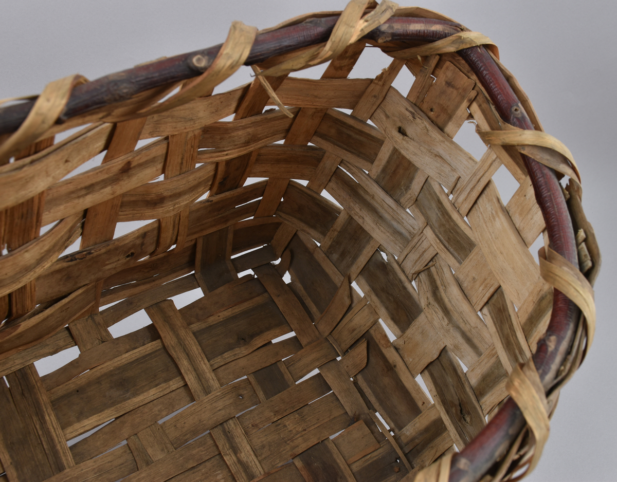 Korg i rakflätad spån. Kantens vidja är lindad. Rektangulär form med flätad botten.