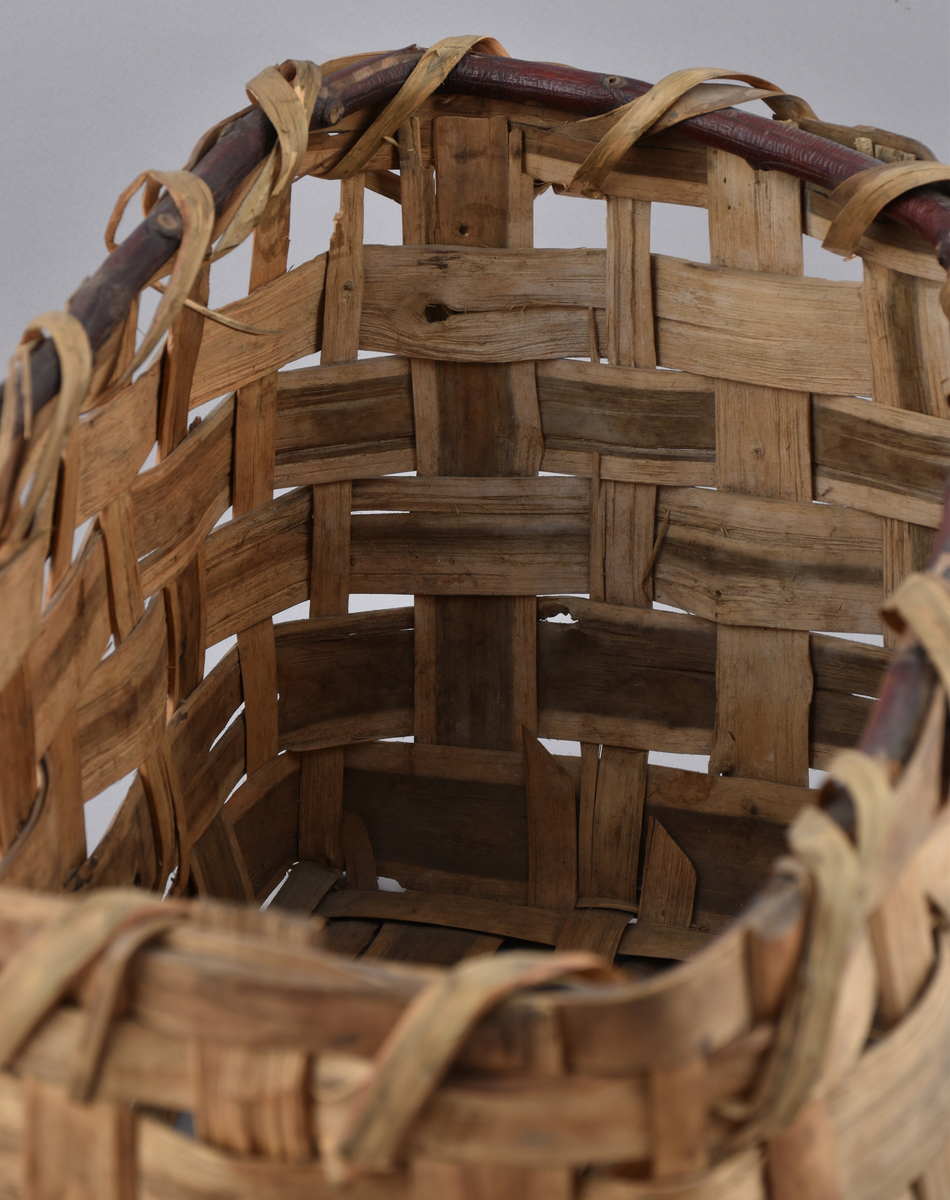 Korg i rakflätad spån. Kantens vidja är lindad. Rektangulär form med flätad botten.