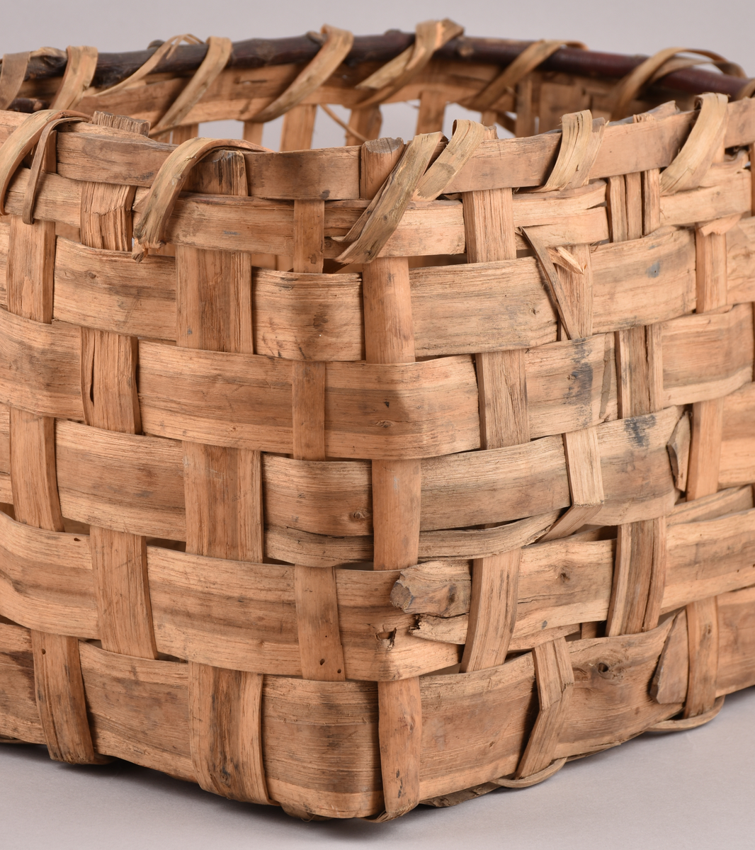 Korg i rakflätad spån. Kantens vidja är lindad. Rektangulär form med flätad botten.