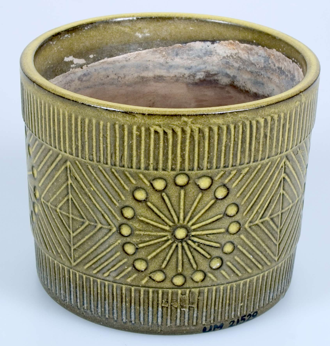 Cylindrisk ytterkruka, grönglaserad med geometriskt ristad dekor och en något markerad kant upptill. Brungrå, oglaserad inuti. Runt hål i botten. Stämplad: UE Sweden 43135/121 ms.