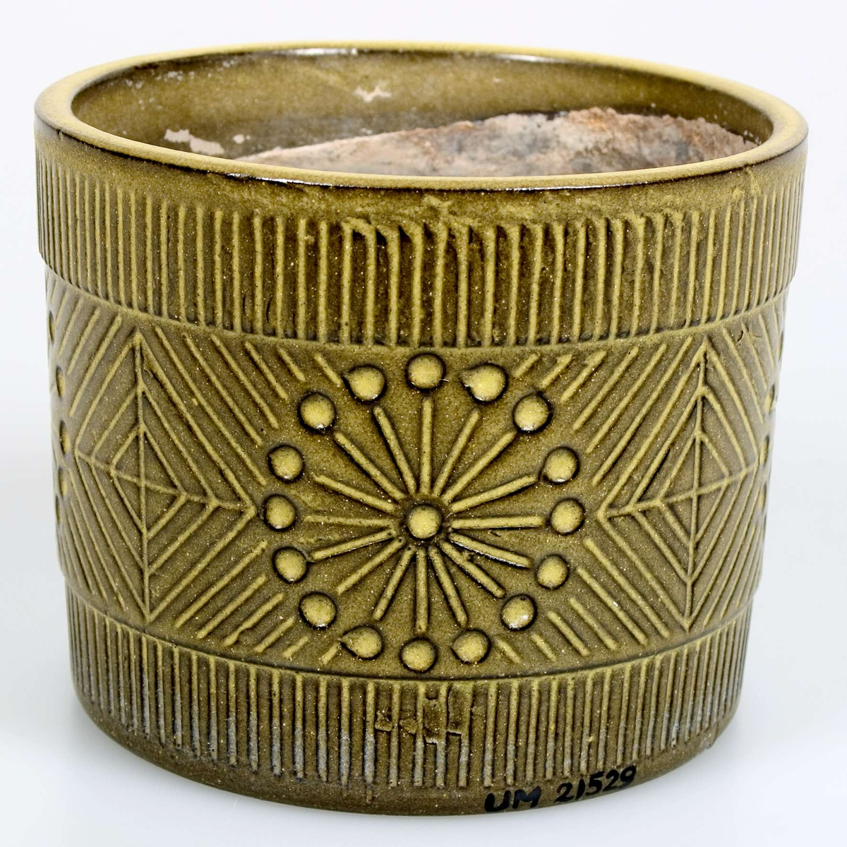 Cylindrisk ytterkruka, grönglaserad med geometriskt ristad dekor och en något markerad kant upptill. Brungrå, oglaserad inuti. Runt hål i botten. Stämplad: UE Sweden 43135/121 ms.