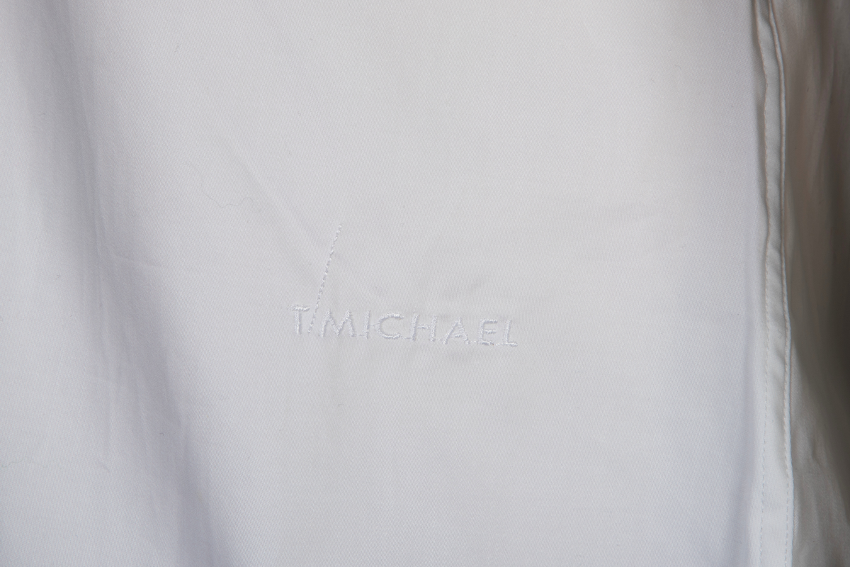 Hvit herreskjorte av bomullssateng. Betegnes som "hand grade", dvs. delvis håndarbeid selv om den er maskinsydd. Talllrike detaljer gjør skjorten meget spesiell: ettsøms ermer flankert av sydde legg og med doble, fôrede mansjetter isatt knuteformede mansjettknapper av hvit, elastisk, silkelignende snor. Innvendig knappestolpe à la smokinskjorte midt foran, men i motsetning til smokingskjorten, synes den ikke på retten. Skjorten lukkes med fem kuleformede, løse knapper, som har flat bakside og kan vendes. Den øverste sitter i halslinningen. De to nederste knappene er vanlige perlemorsskjorteknapper. Skjortens rygg har bærestykke og nedenfor to horisontale, sydde legg. På venstre side har den også et vertikalt "pyntelegg". Skjorten kan bæres med to ulike løssnipper og linningen har derfor fem små knapphull for feste av snipp. Alle vanlige sømmer er en slags indresøm.