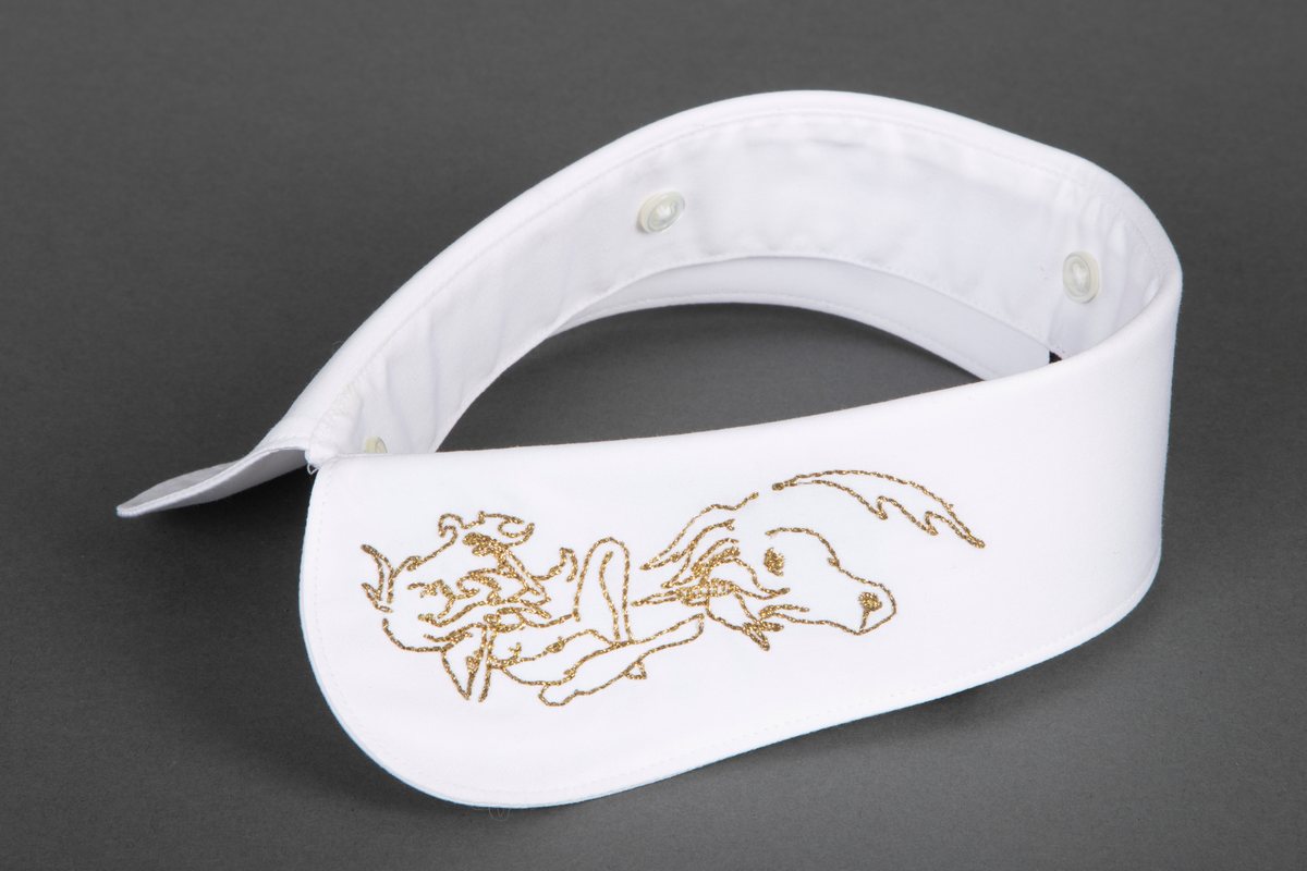 Løssnipp, innvendig fôret med avrundede snipphjørner. Forsiden er prydet på begge snipper med kjedestingsbroderi i gulltråd, mens baksiden er ensfarget hvit. Broderiet forestiller et enhjørningshode under en sittende kvinnefigur, som ser ut til å spille en fele. På kragestanden er påsydd fem små knapper til å kneppe på skjortens halslinning.