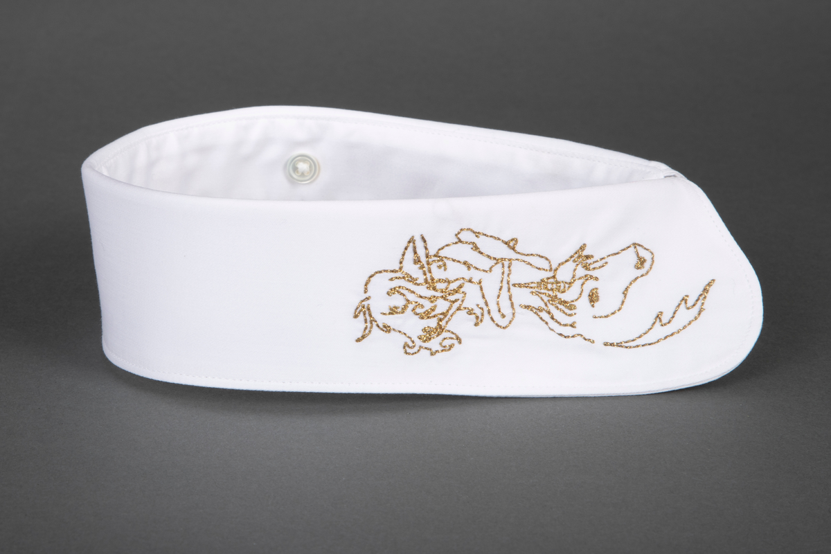 Løssnipp, innvendig fôret med avrundede snipphjørner. Forsiden er prydet på begge snipper med kjedestingsbroderi i gulltråd, mens baksiden er ensfarget hvit. Broderiet forestiller et enhjørningshode under en sittende kvinnefigur, som ser ut til å spille en fele. På kragestanden er påsydd fem små knapper til å kneppe på skjortens halslinning.