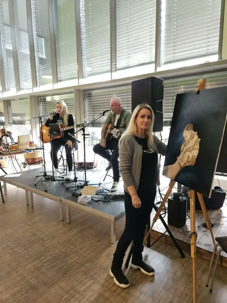 To musikarar og ei dame ved staffeli og måla bilete av eit lite barn 