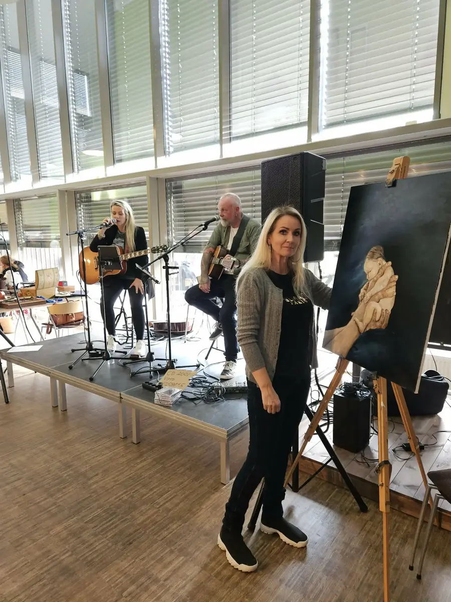 To musikarar og ei dame ved staffeli og måla bilete av eit lite barn 