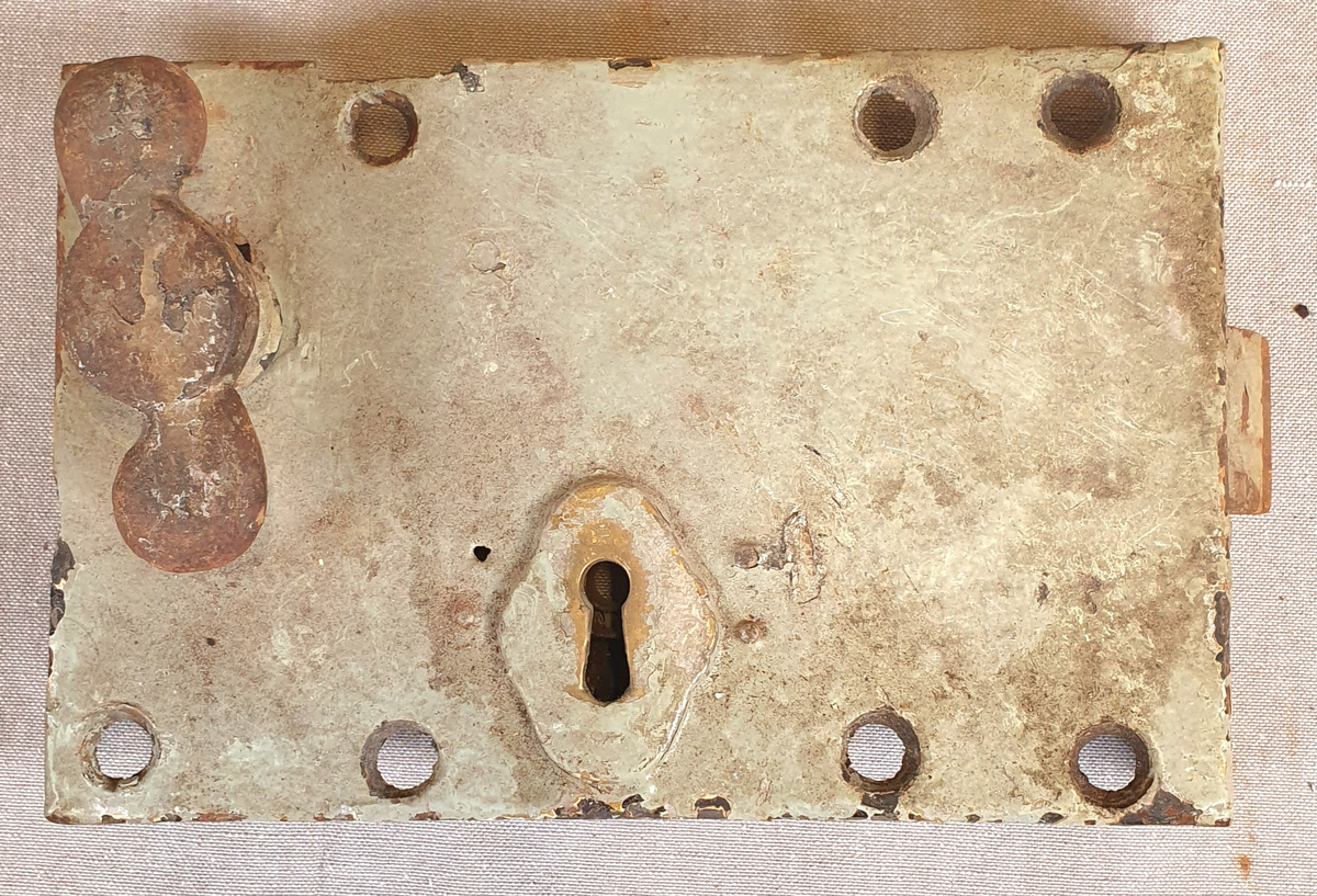 Seks dørlåser av jern. Alle låsene har nøkkelhull og dørvrider. Rammen er tilnærmet kvadratisk og har også hull for feste, samt en list på to paralelle sider, der en mangler. Har en tilhørende nøkkel. Det følger med en ramme i jern i samme stil, trolig til en dørluke.