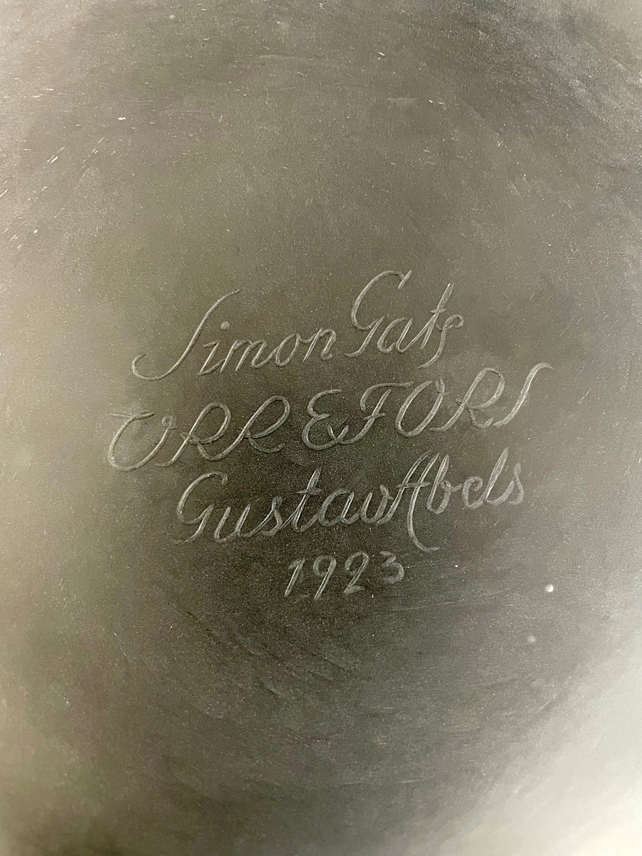 Formgiven av Simon Gate, gravyrarbete utfört av Gustav Abels. "Oxhuvudena", stor urna (eller pokal) med lock. Gravyr med motiv består av fyra scener, samtliga innehållande kvinnor i olika scener, och i en scen finns även ett barn. Dessa motiv ramas in av fyra graverade pelare, vilka uppåt avslutas med en mytologisk gestalt. Locket graverat motiv bestående av tjurhuvuden i fyra grupper om två eller tre stycken huvuden. Mellan dessa människogestalter med svärd som sticks ner i marken. Överst en knopp i form av en plym.