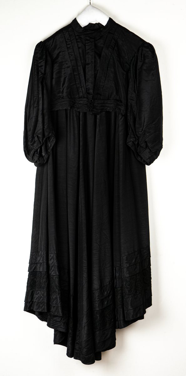 a, Klädning av svart alpackasiden. Prydd med bårder i svart.
b, garnering till livet.
c, kjol med bård och veck som pryder kanten.