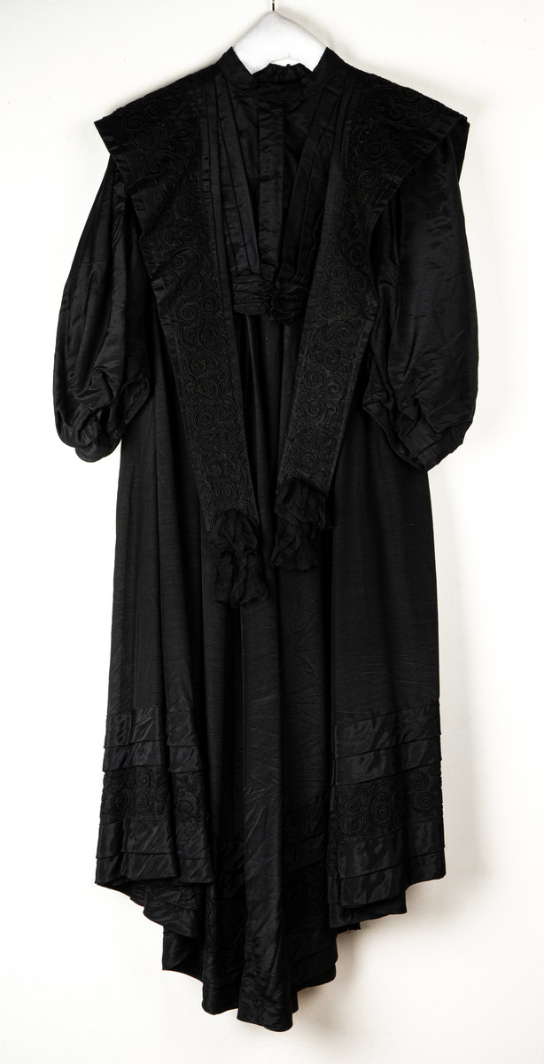 a, Klädning av svart alpackasiden. Prydd med bårder i svart.
b, garnering till livet.
c, kjol med bård och veck som pryder kanten.