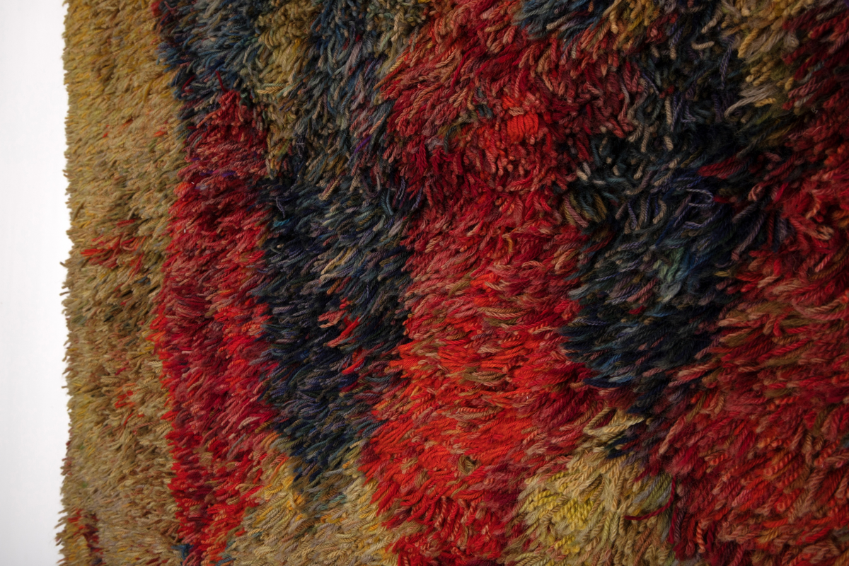 Rektangulær rye i ullfloss med rombemotiv. Tette rekker innknyttet langtrådet floss av løst tvunnet, tykt ullgarn med cirka 1 cm avstand mellom rekkene. Flossens hovedfarge er gullig (gult og nyanser av beige og grønt) med svake innslag av mønsterfargene; nyanser av rødt og blått. Disse er samlet i ujevne, rombiske figurer i rekker. En bred kant uten floss, i bunninnslagets gullige farge avslutter ryen oppe og nede.