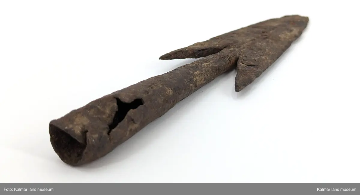 Järnålder. Bred spjutspets av järn med hullingar. Rund holk, något skadad.